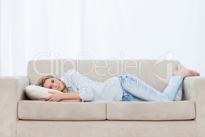 A woman is lying on a couch resting her head on a pillow