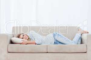 A woman is lying on a couch resting her head on a pillow