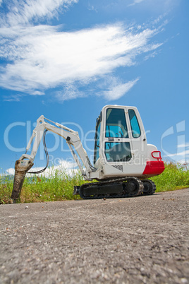 Small caterpillar tractor stands on the asphalt against the blue