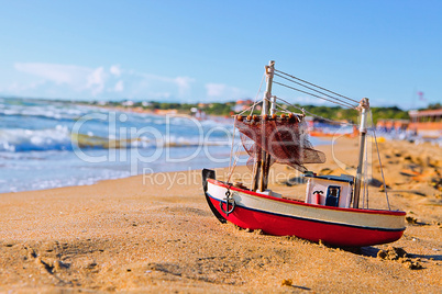 The little toy boat stands on sandy beach