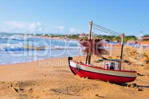 The little toy boat stands on sandy beach