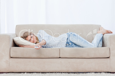 A woman lying on a couch resting is holding a television remote