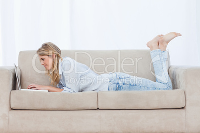 Side view shot of a woman lying on a couch using her laptop