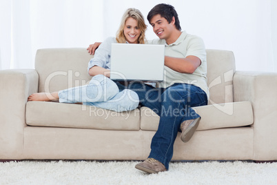 A smiling couple are sitting on a couch together looking at a la