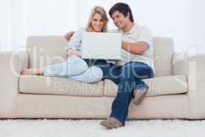 A smiling couple are sitting on a couch together looking at a la