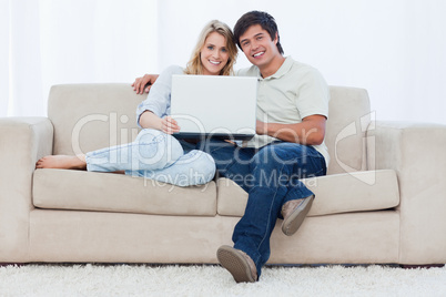 A smiling couple with a laptop are looking at the camera