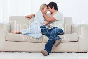 A couple are sitting on a couch looking at each other with their