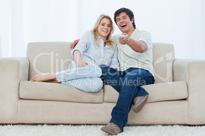 A young couple are sitting down looking at the camera and laughi