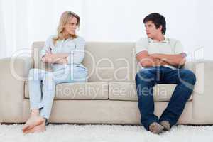 A couple sit at the two ends of the couch with their arms folded