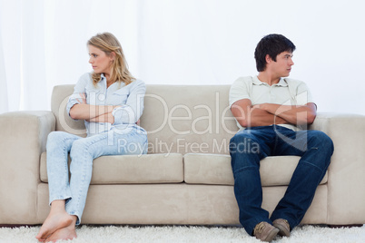 A couple sit at the two ends of the couch with their arms folded