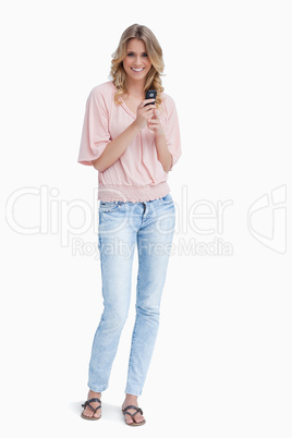 A woman is standing smiling at the camera and holding a mobile p