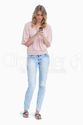 An angry woman standing looking at her mobile phone