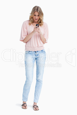 A surprised woman is standing looking at her mobile phone