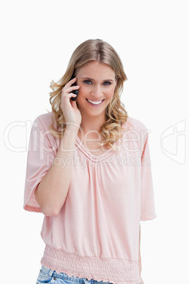 A woman smiling at the camera has her mobile phone up to her ear