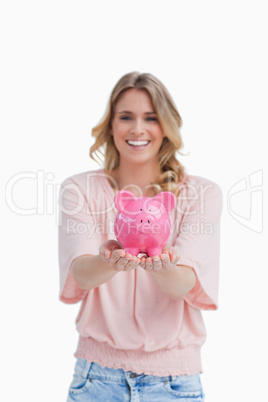 A smiling woman is holding a piggy bank in the palms of her hand