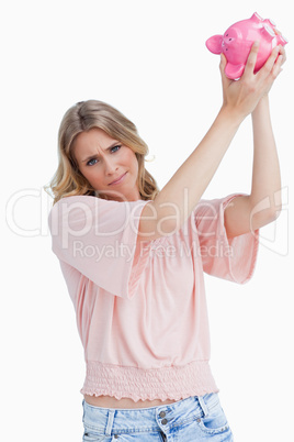 Disappointed woman holds a piggy bank up over her head