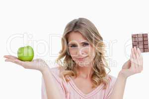 Young blonde woman holding an apple and a chocolate bar