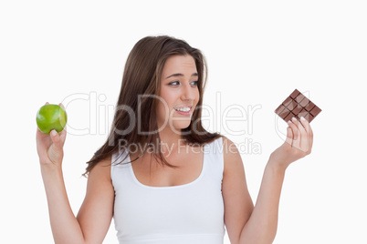 Young brunette woman holding a piece of chocolate and an apple