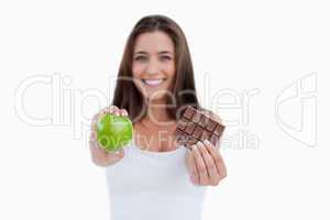 A green apple and a piece of chocolate being held by a woman
