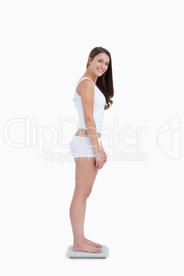 Smiling woman standing on weighing scales while looking at the c
