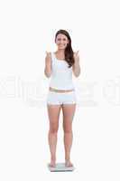 Smiling woman placing her thumbs up while standing on weighing s