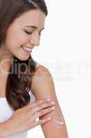 Peaceful brunette applying some cream on her arm