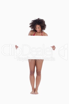 Young woman looking down while pointing a blank poster