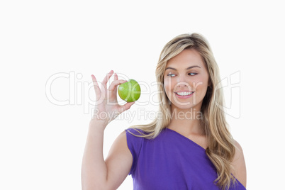 Happy young blonde woman looking at a green apple