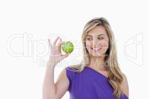 Happy young blonde woman looking at a green apple