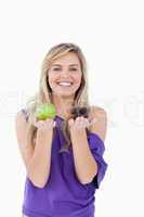 Smiling blonde woman hesitating between a muffin and an apple