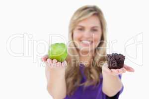 A fruit and a muffin being held by a blonde woman
