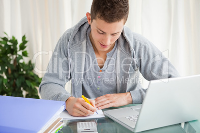 Smiling student doing his homework with a laptop