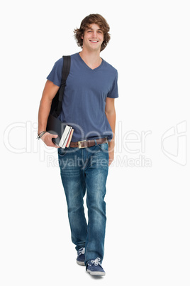 Front view of a male student walking with a backpack and books