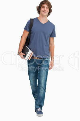 Front view of a student walking with a backpack and books