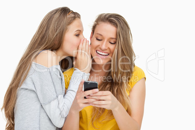 Young woman whispering to her friend who's texting on her phone