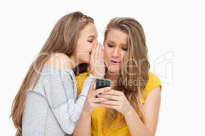 Student whispering to her friend who's texting on her phone