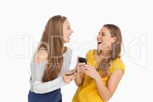 Two young women laughing while holding their cellphones