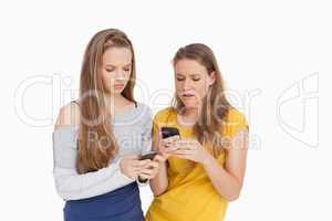Two young women frowning while looking their cellphones