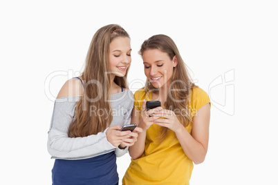 Two young women smiling while looking their cellphones