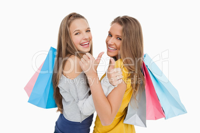 Rear view of two young women the thumb-up with shopping bags