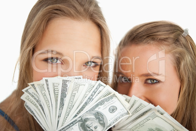 Close-up of two young woman behind dollars