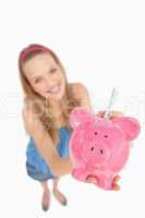 Fisheye view of a young woman putting money in a piggy-bank