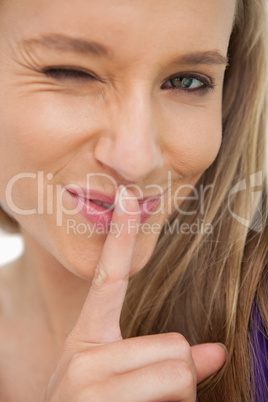 Green-eyes young woman winking with a finger on the lips