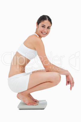 Slim young woman smiling while sitting on a scales