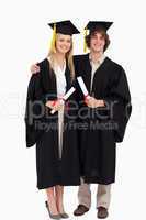 Two students in graduate robe shoulder to shoulder