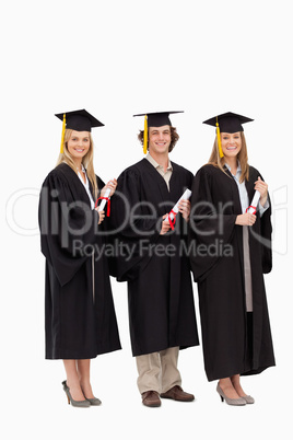 Three smiling students in graduate robe holding a diploma