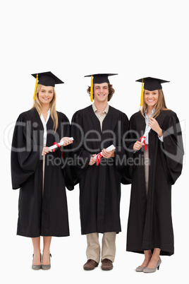 Three students in graduate robe holding a diploma