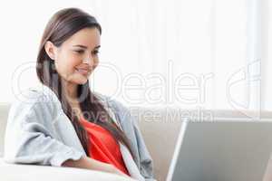 A smiling woman using her laptop as she relaxes on the couch