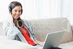 A smiling woman holding headphones and a laptop while looking at