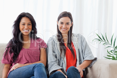 Two smiling women sit on the couch together while looking at the